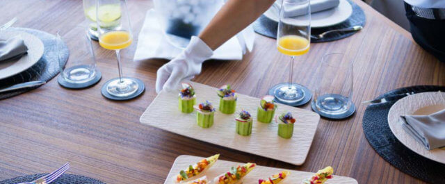 	Photo en plongée sur une table dressée pour un repas et où une personne sert des mets haut de gamme
